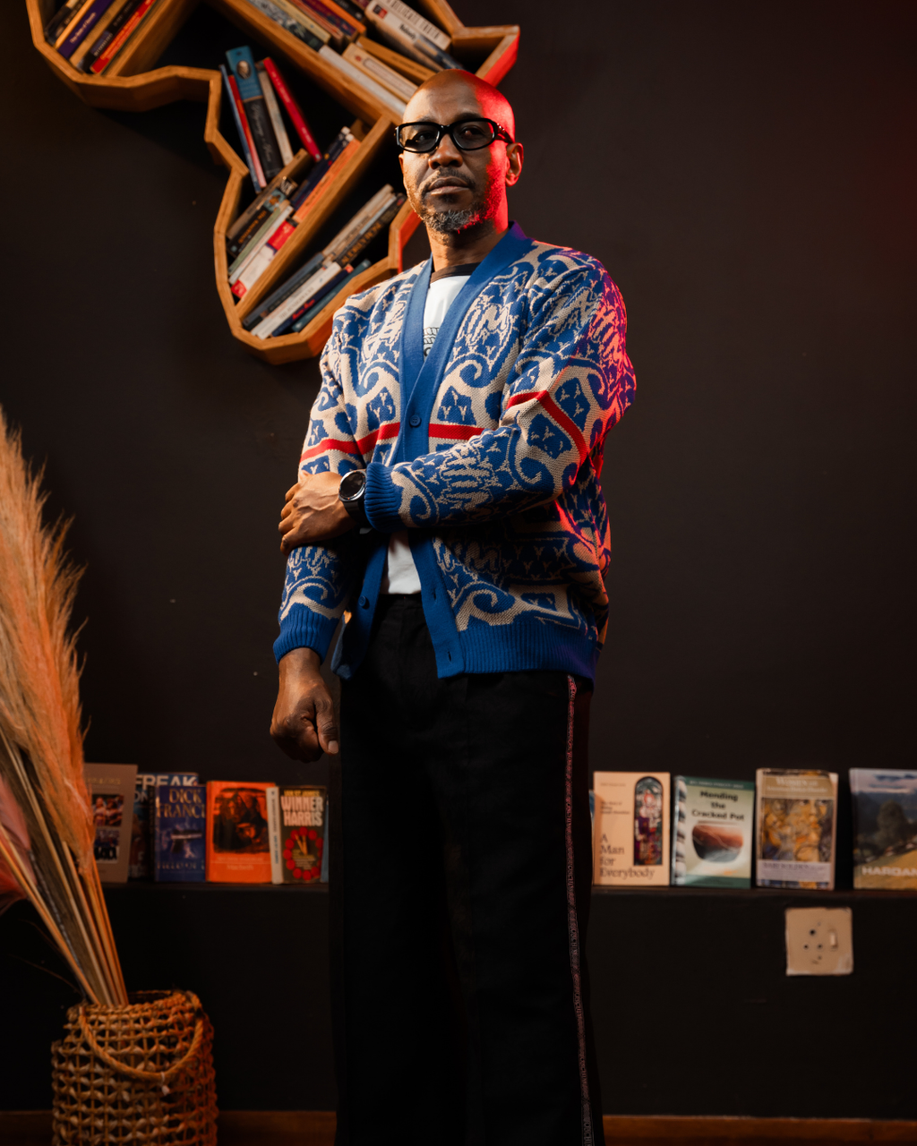 Man wearing a colorful cardigan in a room with books and decor.