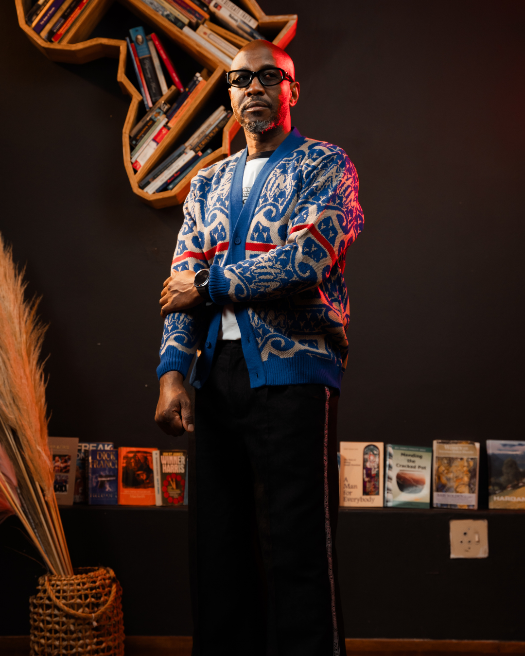 Man wearing a colorful cardigan in a room with books and decor.